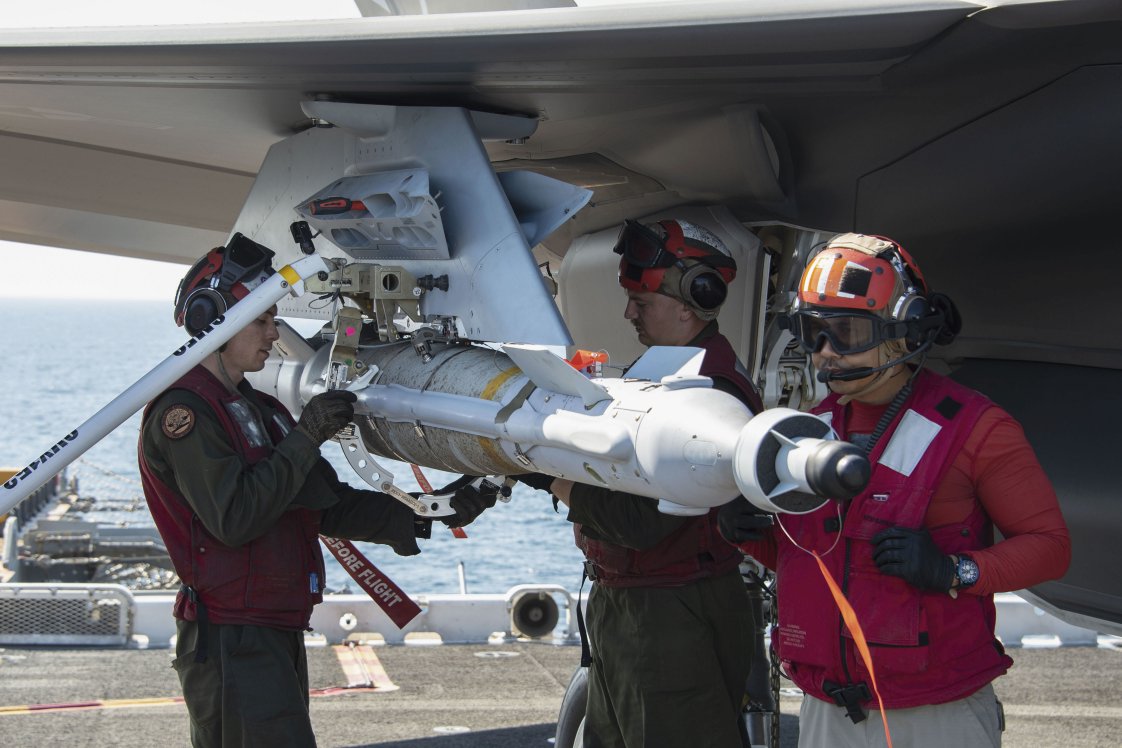 
        A GBU 49 is loaded onto an F-35B on the flight deck of Wasp-class amphibious assault ship USS
        Essex
        (LHD 2) on 12 December 2018. The USN modified an adapter, the white collar being removed by USMC Corporal Randle Lane (left), to load GBU-49 on the F-35B because the weapon’s conduit did not fit the current weapons loader.
       (USN)